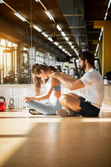 Sticker - Side view of attractive beautiful sporty muscular shape couple sitting in front of the mirror while man massaging his girlfriend in the sunny gym.