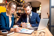 © rh2010 - Caucasian business couple dressed strictly in the suits working together with laptop and paper charts sitting at the cafe during the coffee break