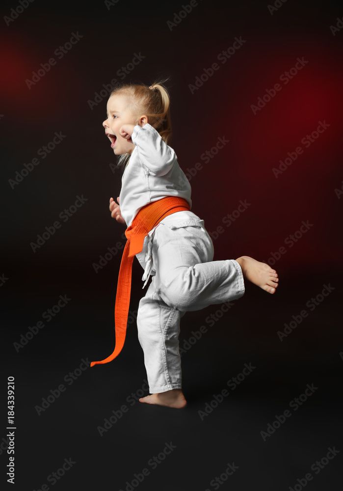 Little girl practicing karate on dark background