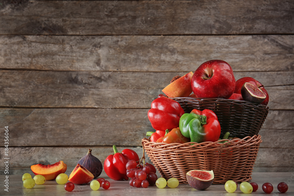 Basket with different fruits and vegetables against wooden background