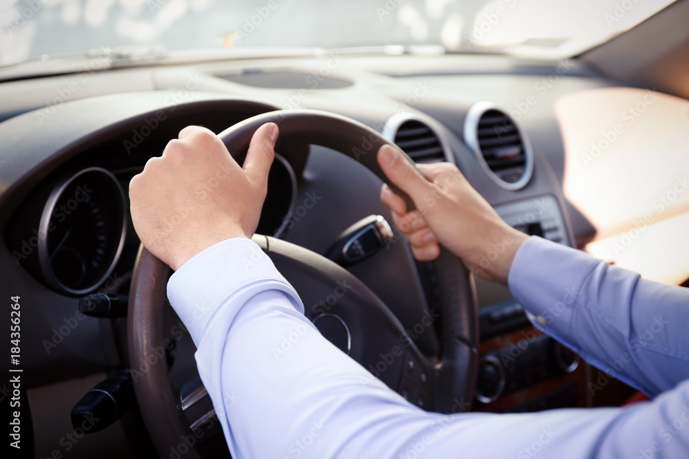 Young man holding hands on steering wheel of car