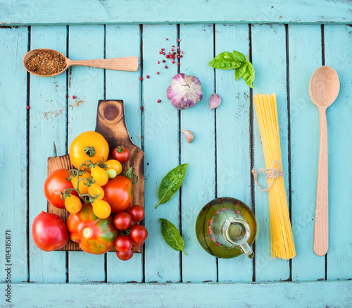 Foto-Schmutzfangmatte - Ingredients for cooking on rustic shabby chic wooden table. Tomatoes on wooden  cutting board, pasta, basil, garlic, olive oil and spices in wooden spoon. Healthy food concept. (von Polina Ponomareva)