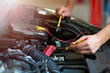 © pikselstock - Auto mechanic checking car battery voltage