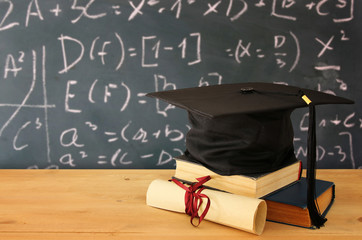 Image of graduation black hat over old books next to graduation on wooden desk. Education and back to school concept