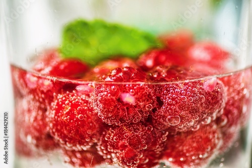 Fotografia, Obraz Glass with many raspberry in water with bubbles.