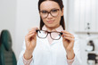 © LIGHTFIELD STUDIOS - selective focus of ophthalmologist holding pair of eyeglasses in hands in clinic