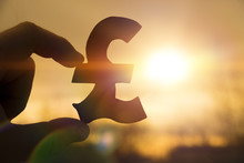 Silhouette Symbol Of The British Pound Sterling In Hand Against The Background Of The Dawn