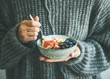 Healthy winter breakfast. Woman in grey woolen sweater eating rice coconut porridge with figs, berries and hazelnuts. Clean eating, vegetarian, vegan, alkiline diet food concept