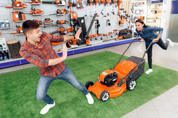 Wall Mural - A girl and a guy are posing with a lawn mower in a tool store.