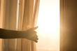 © StudioN - Female arm reaching out to open a curtain - warm sun light shining through