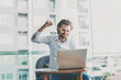 © Thomas - Casual dressed white business man celebrate with laptop. Education or technology or startup business concept, modern office or living room with copy space