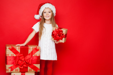 Happy smiling girl in a Christmas cap holding a gift in a craft paper with red bow on a red background. Girl with big gift box. Merry Christmas. Shopping. Black Friday. Discount