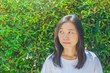 © Angkana - Portrait Asian woman wearing whit t-shirt and thinking something. She looking at right side hand with green bush in the background.
