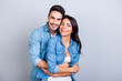 Portrait of cheerful lovely cute couple with beaming smiles hugging and looking at camera over grey background