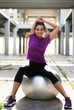Young beautiful athlete girl sitting on silver pilates ball  in an old abandoned building outdoor