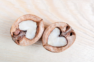 Two halves of walnut in shape of heart are lying side by side on a light wooden table.