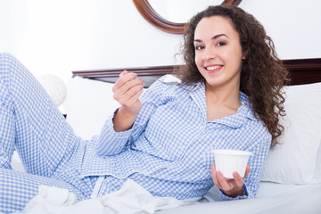 Wall Mural - Curly haired woman with tasty yoghurt in bed