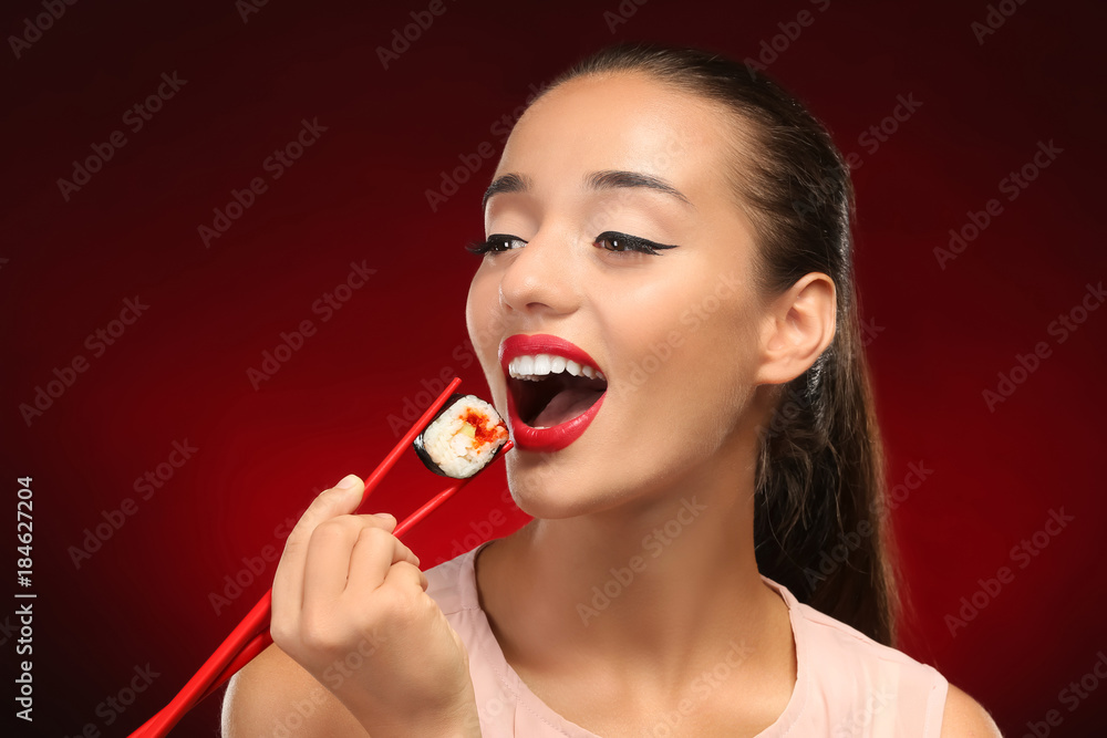 Beautiful young woman with sushi roll on color background