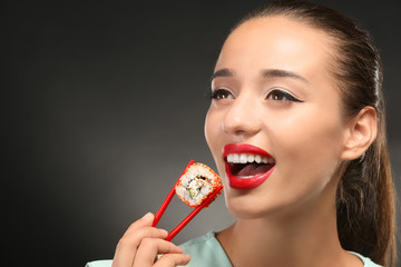 Beautiful young woman with sushi roll on grey background