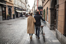 Young Couple Walking On The Streets Of A Lovely Little City With A Bike