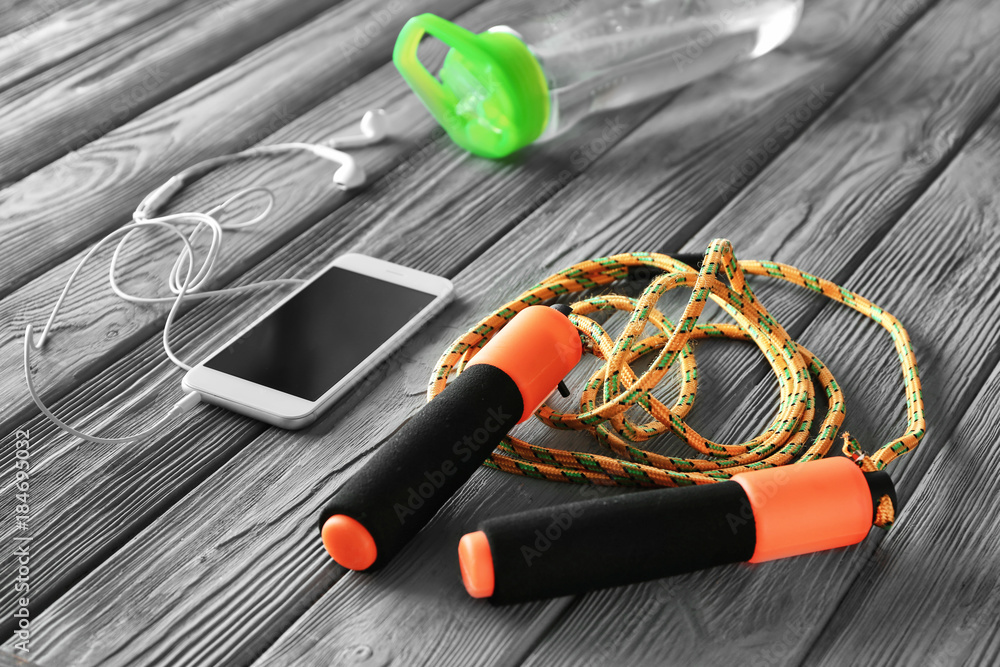 Jumping rope and smartphone on wooden background