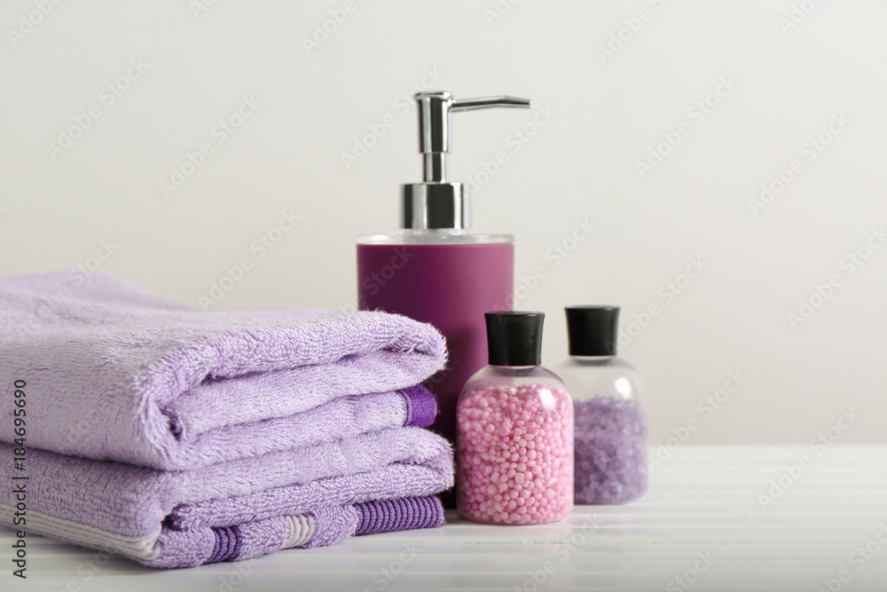 Clean towels and cosmetics on table against light background