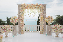 Elegant Wedding Arch With Fresh Flowers, Vases On Background Of Ocean And Blue Sky.
