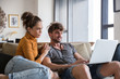 © Jovo Jovanovic/Stocksy - Smiling couple with laptop sitting on sofa