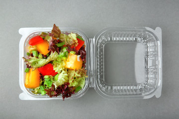 Plastic container with salad on grey background