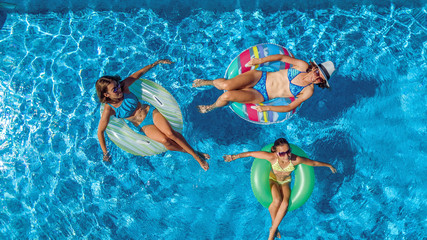 Wall Mural - Aerial top view of family in swimming pool from above, happy mother and kids swim on inflatable ring donuts and have fun in water on family vacation
