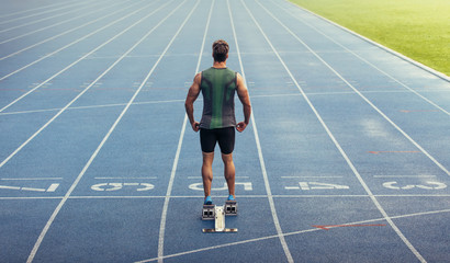 Wall Mural - sprinter standing on starting block on running track