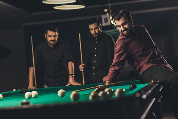 company of young successful handsome men playing in  russian pool at bar