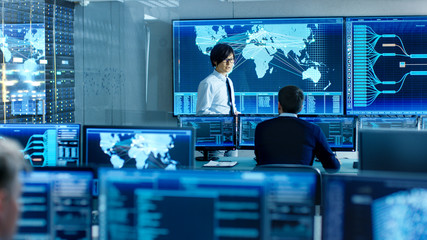 Leinwandbilder - In the System Control Room Chief Engineer Holds a Briefing for Member of the Staff. They're Work in Data Center and are Surrounded by Multiple Screens Showing Maps, Logistics Data.
