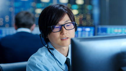 Poster - In the Network Operations Center Senior Trader Teaches Young Associate to Makes Personal Client Call with a Headset. They're Surrounded by Monitors Showing Data and Graphs.