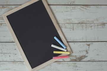 Clean and empty framed blackboard with colorful chalks on wooden background. Chalkboard on gray table. Back to school concept