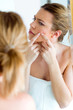 © nenetus - Beautiful young woman removing pimple from her face in a bathroom home.