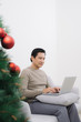 Man with laptop while sitting on couch next to christmas tree