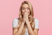 Beautiful Excited Blonde Female Covers Eyes With Happiness, Doesn`t Expect To Recieve Pleasant Surprise From Close Friend, Being Thankful And Pleasantly Shocked, Isolated Over Pink Background