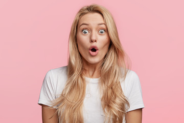 Wall Mural - Pretty blonde woman stares at camera, keeps mouth widely opened, dressed in casual t shirt, expresses great surprisment, feels shocked about sales in web sites, wines in online contest, wonders news