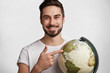 © wayhome.studio  - Handsome cheerful young active bearded traveller holds globe, chooses destination where to go, indicates at different continents, makes important choice. People, travelling and adventure concept
