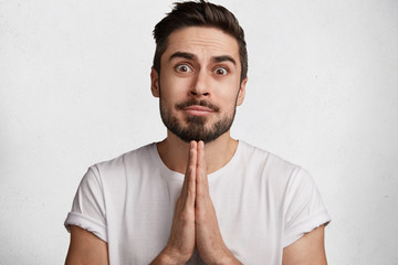 Wall Mural - Portrait of handsome bearded male has pleading expression asks girlfriend to go in cafe or restaurant with him, wants to spend free time with lover. Attractive young man demands forgiveness.