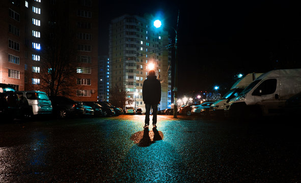 Fototapete - a mysterious man stands alone in the street, among cars in an empty city, weat road after the rain, walks the night street, dreams