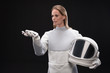 No connection. Serious young spacewoman is standing in protective suit while holding helmet and smartphone. She is looking at screen of gadget while expressing disappointment. Isolated