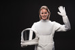 Hello. Portrait of friendly young attractive spacewoman is standing in full armor and holding helmet while waving her hand. She is looking at camera with smile. Isolated with copy space