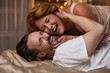 Portrait of excited married couple lying on bed and laughing. They are hugging with closed eyes