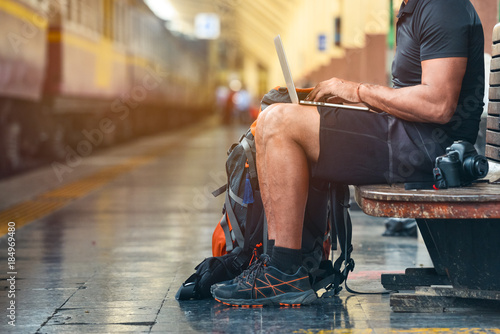 Fotomural Tourist man with a backpack in the train station working on a laptop