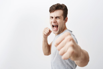 Wall Mural - Furious outraged caucasian man shouts in anger, frowns his face, keeps fists, going to defend himself in fight with criminals. Desperate european guy dark hair shows his power, clenches fists.