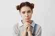 Close up portrait woman with brown hair in double buns pouting with pity look holding hands like praying. Pathetic expressions of girl asking for forgiveness over white wall. Concept of emotions