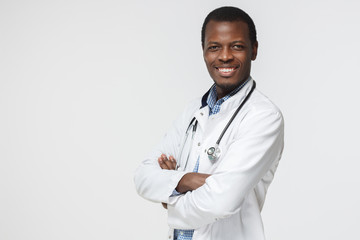 Wall Mural - Smiling african american doctor posing with arms crossed, wearing a stethoscope, isolated on grey background