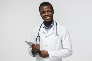 Wall Mural - Indoor closeup of handsome African American doctor isolated on white background dressed in uniform with tablet PC in hands looking at camera with confident positive smile ready to work and help